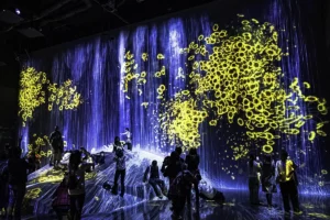People taking pictures in front of yellow flower projections on blue waterfall