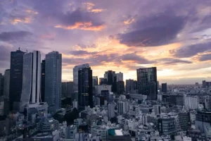 Wide view of a city skyline at sunset, with skyscrapers under a dramatic sky filled with purple and orange clouds.