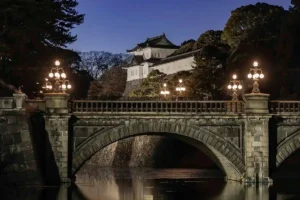 Illuminated stone bridge and traditional yagura at the Tokyo Imperial Palace at night, reflecting in the moat.
