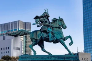 Side profile of the bronze Masashige Kusunoki equestrian statue, set against a backdrop of modern skyscrapers.