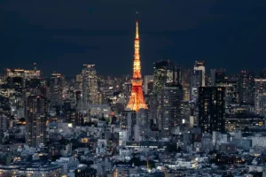 Tokyo skyline at night featuring the iconic, orange-lit Tokyo Tower surrounded by glowing city skyscrapers.